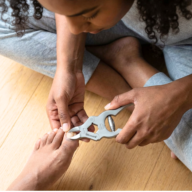 Person using a foot care tool on another person's foot on a wooden floor.